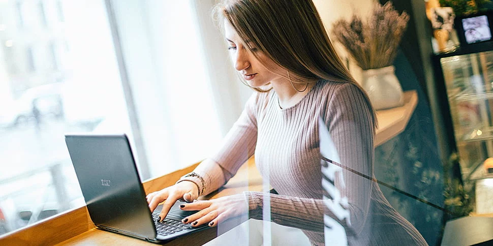 Focused young woman using laptop in a bright, trendy cafe, planning digital content strategy.