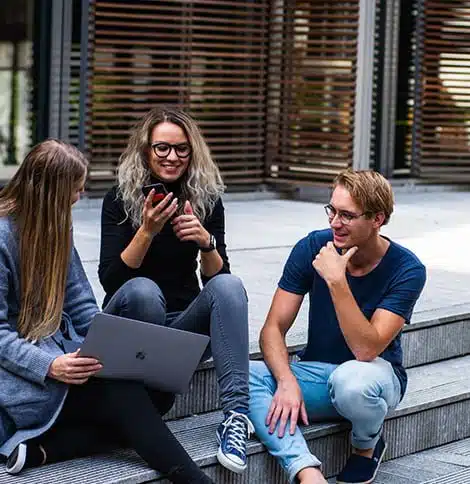 Group of young adults with laptop and smartphone, collaborating outdoors in an urban setting.